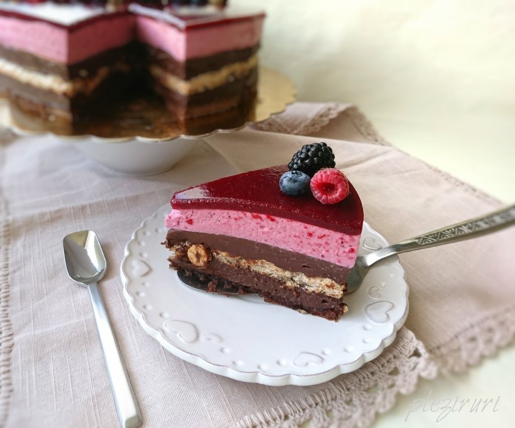 Felie de tort cu ciocolată, alune și fructe de pădure, cu straturi vizibile și glazură de jeleu, decorată cu fructe de pădure proaspete