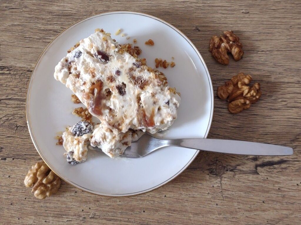 Felie de semifreddo cu nuci caramelizate și stafide, servită pe farfurie, cu nuci alături